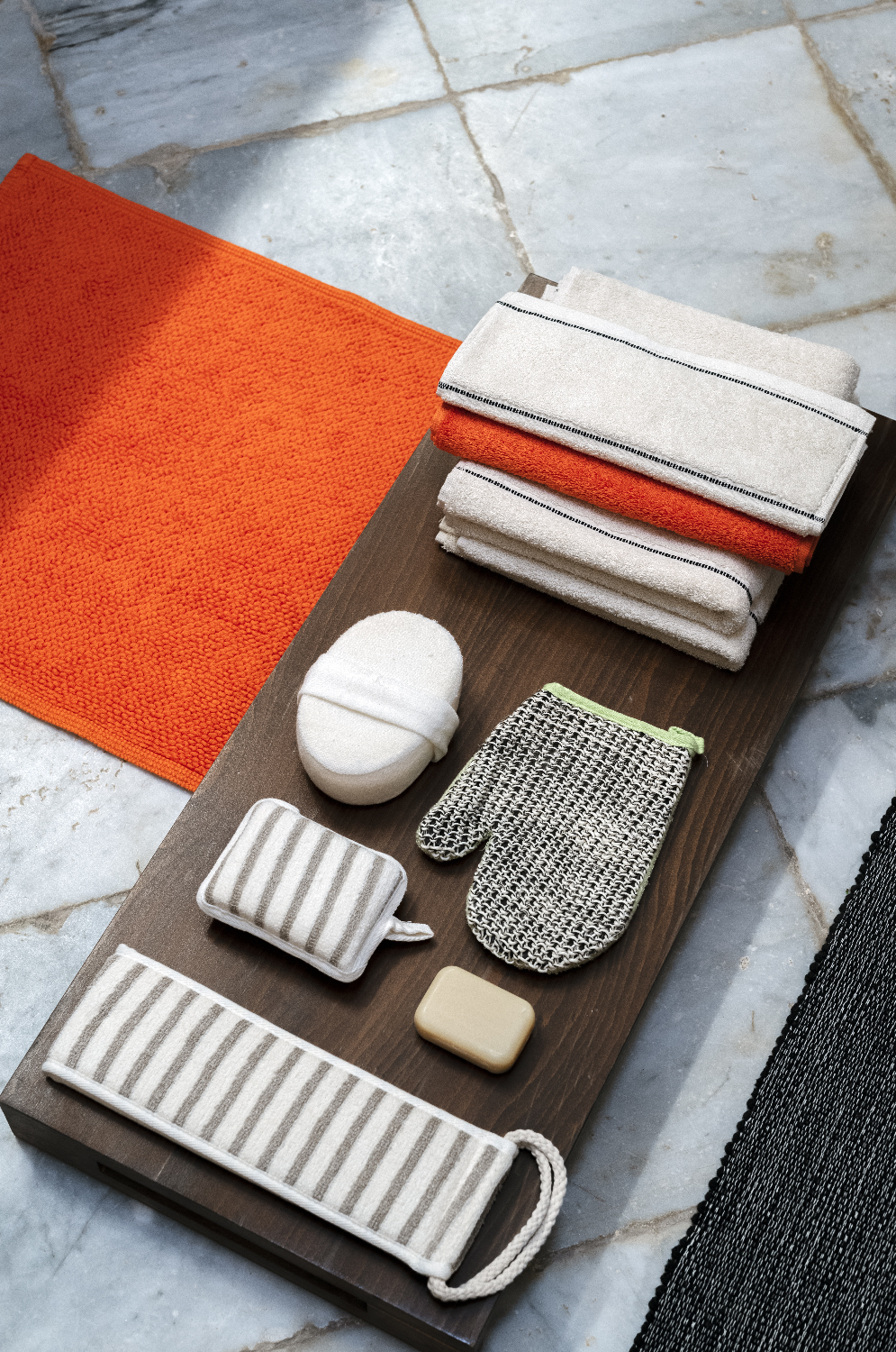 Bath textiles, washing mitt and soap on a wooden board beside an orange bath mat