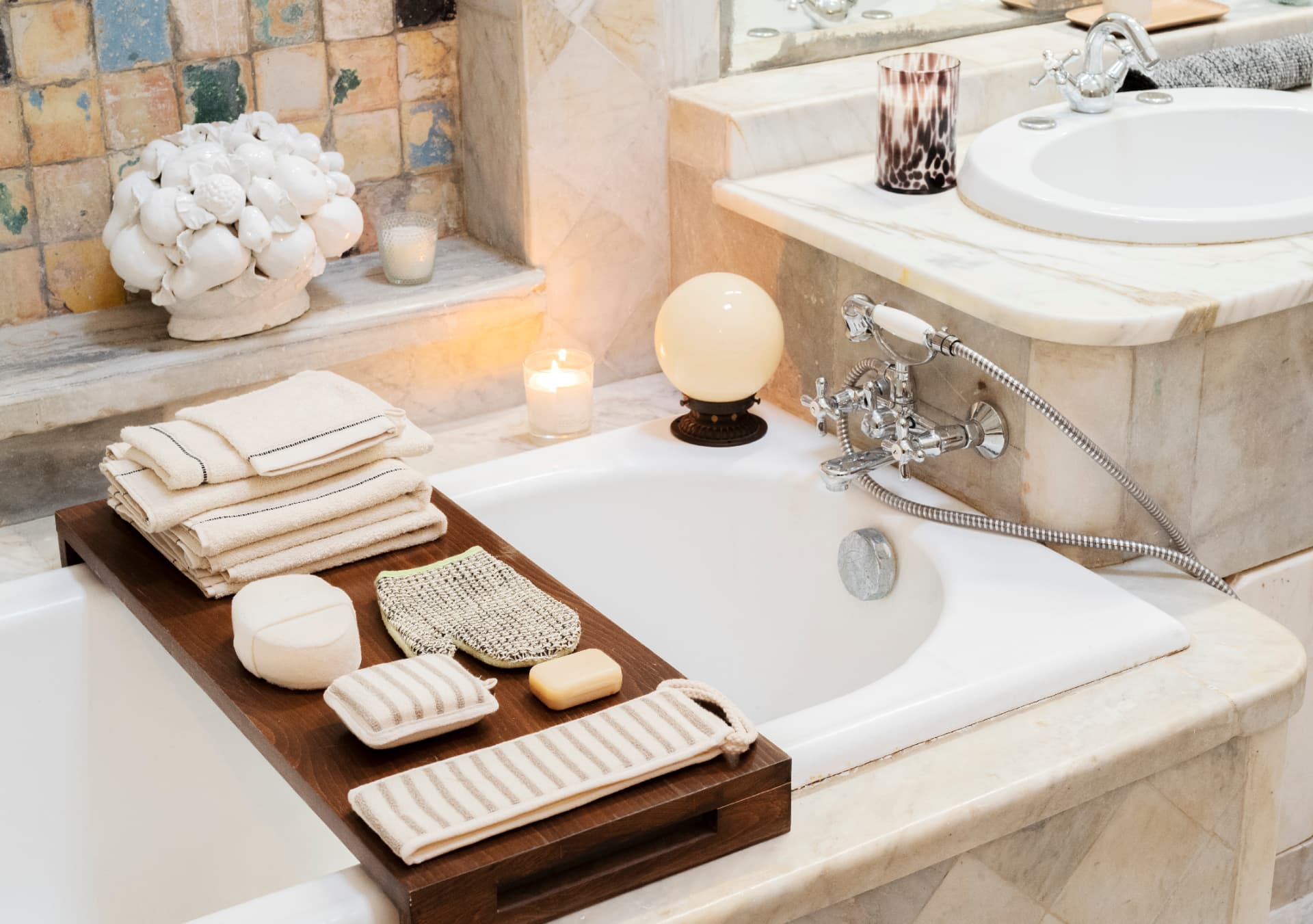 Marble bathroom with towels, soaps and candles arranged on a wooden bath tray