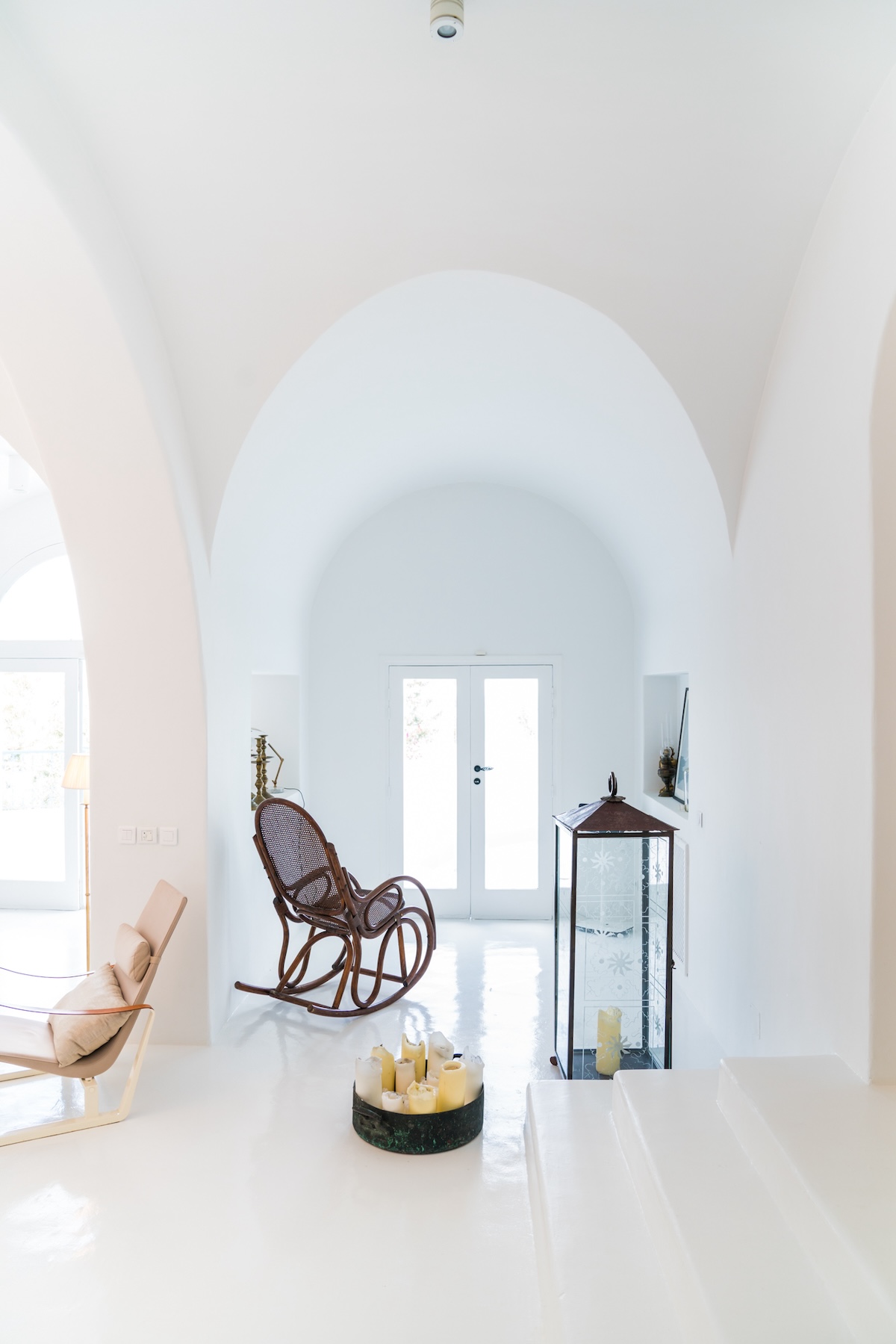 White arched hallway with a dark wood rocking chair and glass doors