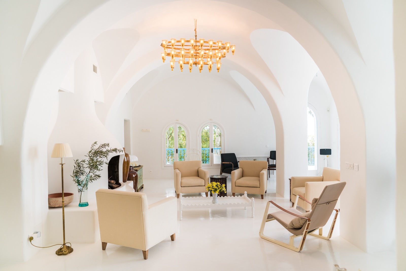 White arched living room with beige armchairs and a brass chandelier