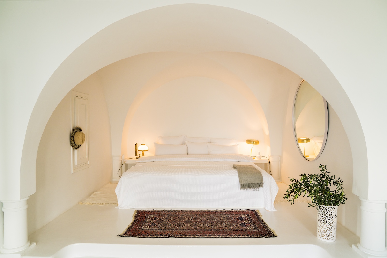 White arched bedroom with a white bed, patterned rug and bedside lamps