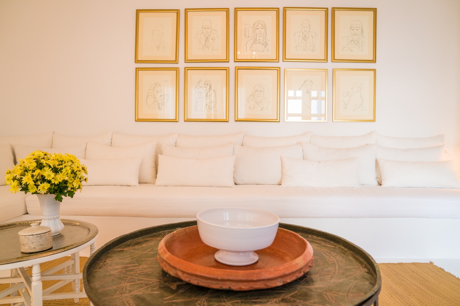 Seating area with a white built-in sofa, gold-framed sketches and round coffee tables