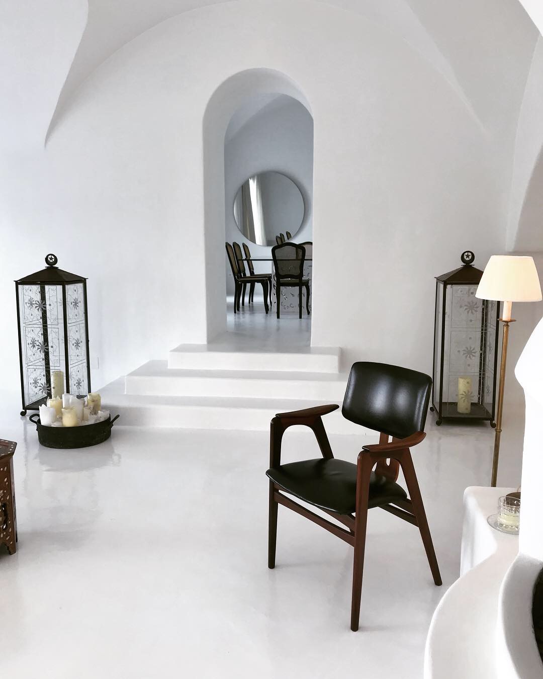 White room with a dark leather armchair, glass lanterns and an arched doorway to the dining area