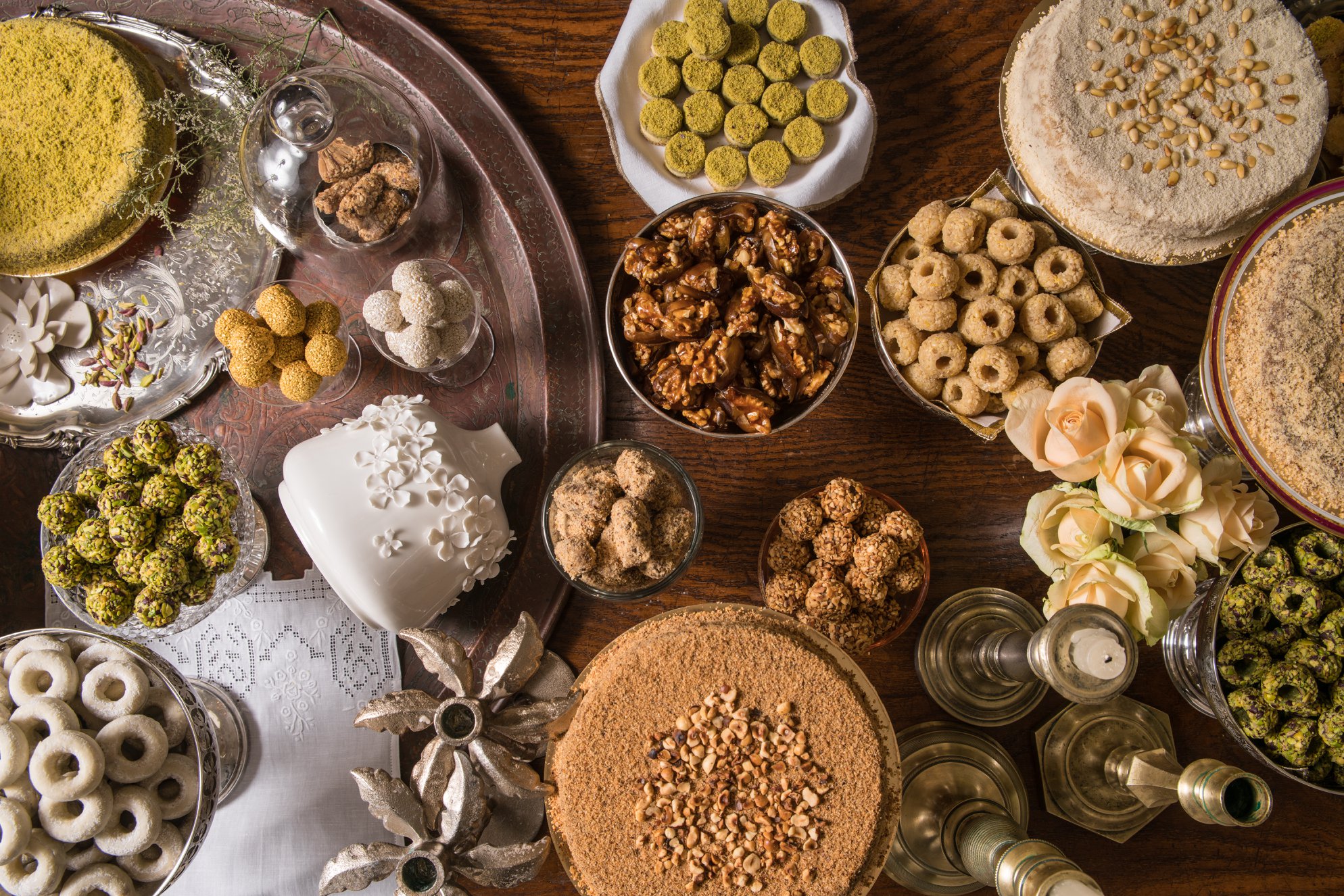 Overhead display of Tunisian sweets with pistachio and nougat cakes, candied walnuts, roses and candlesticks