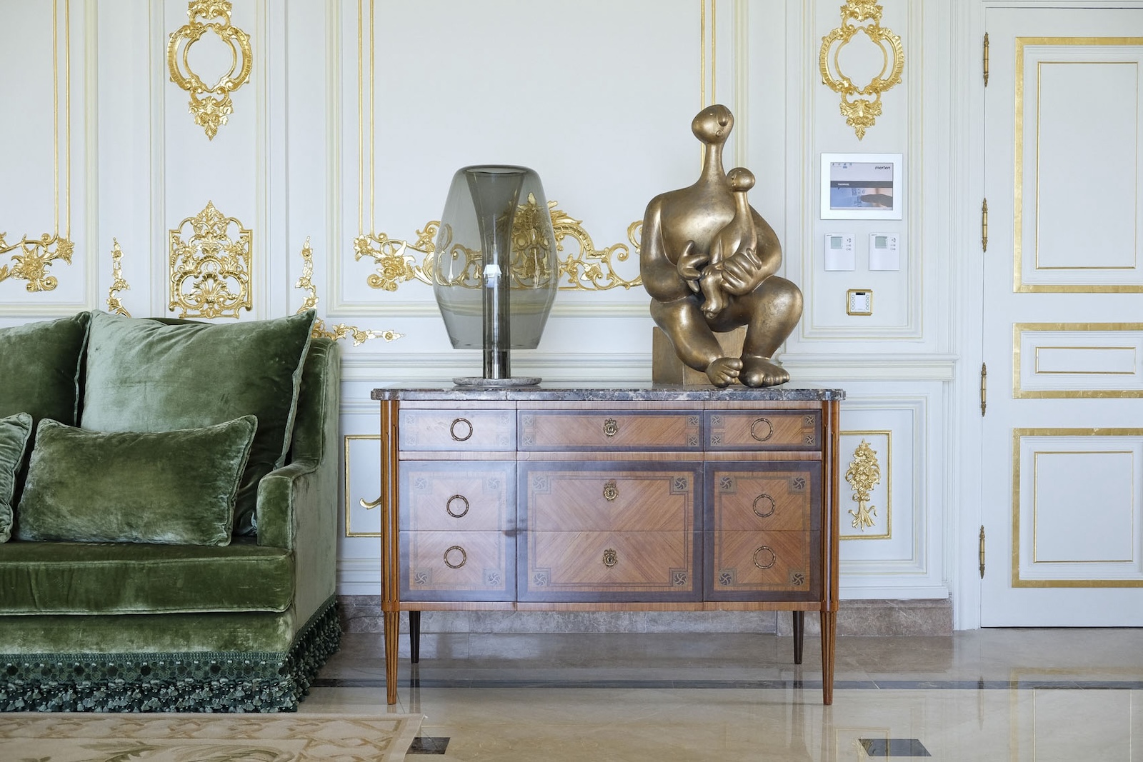 Green velvet sofa and antique commode against gilded wall panelling