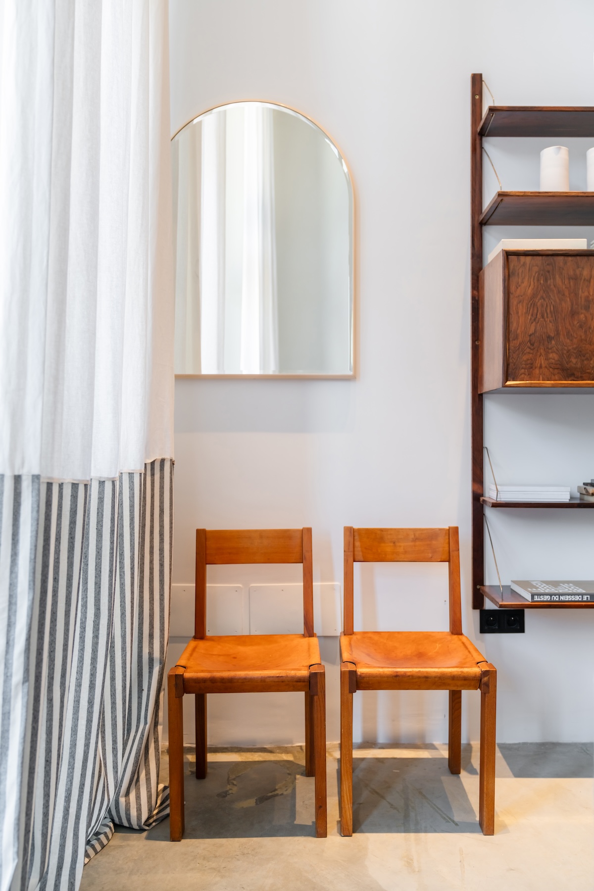 Two cognac leather chairs beneath an arched mirror beside a striped curtain