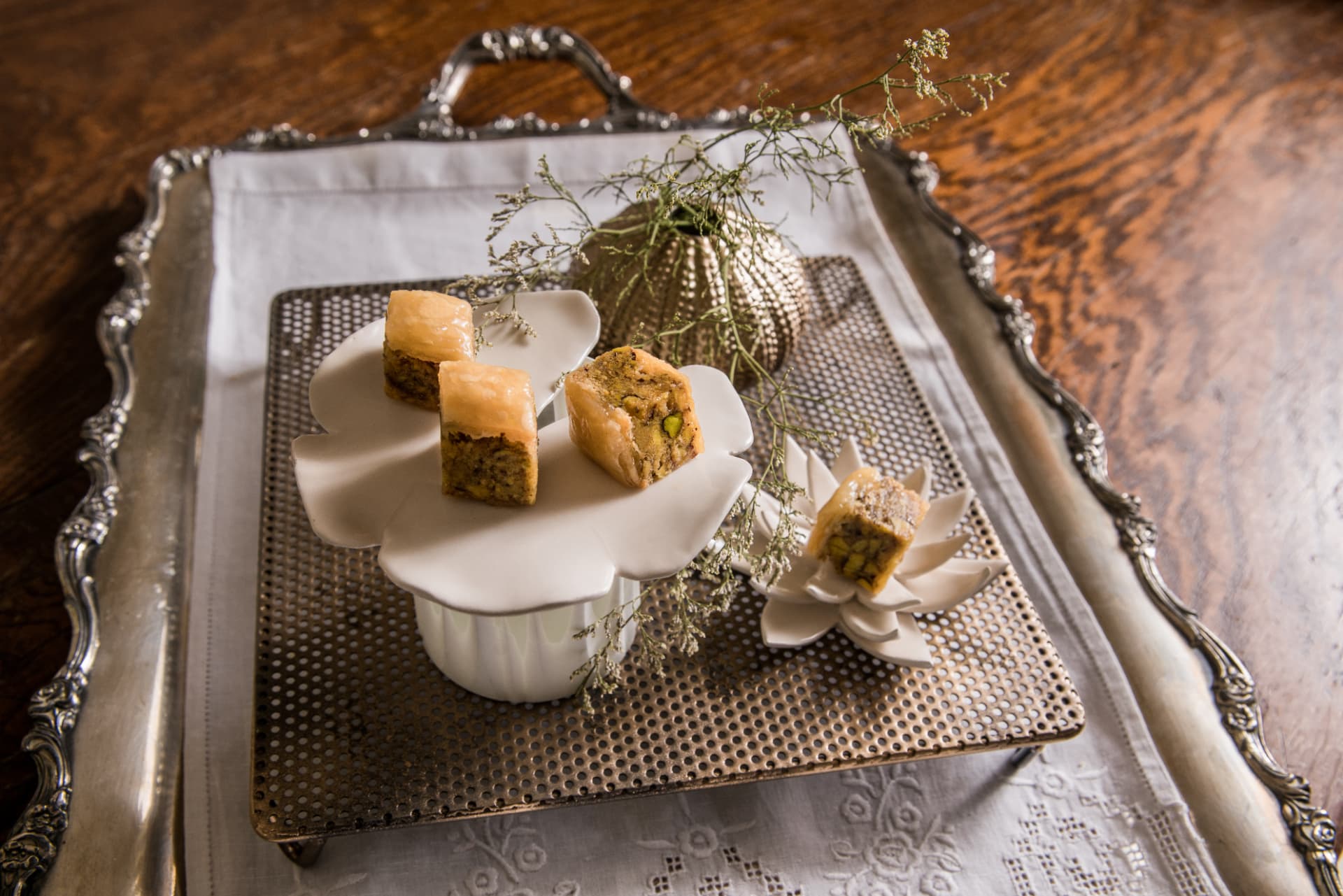 Pistachio pastries served on white ceramic leaf dishes over a silver tray with dried flowers