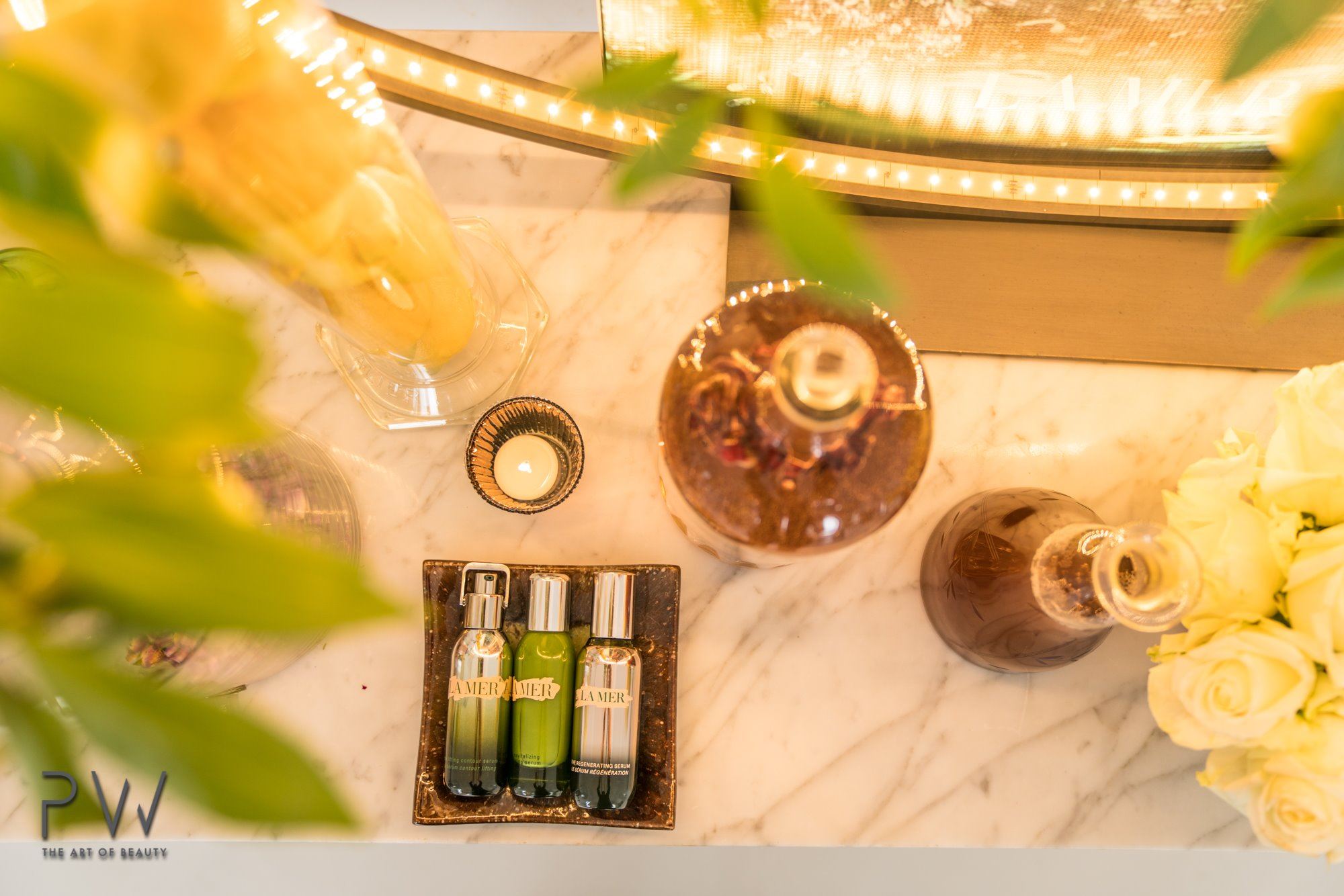 La Mer skincare serums arranged with candles, greenery and white roses