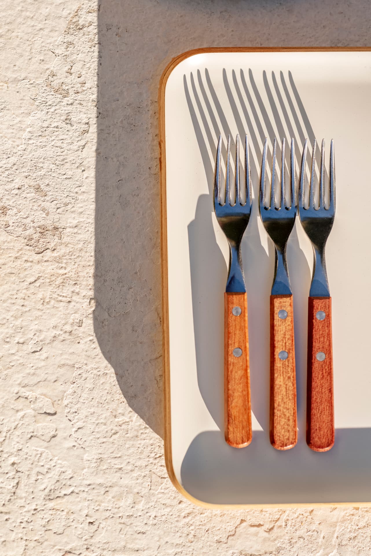 Three wooden-handled forks on a cream tray casting long shadows