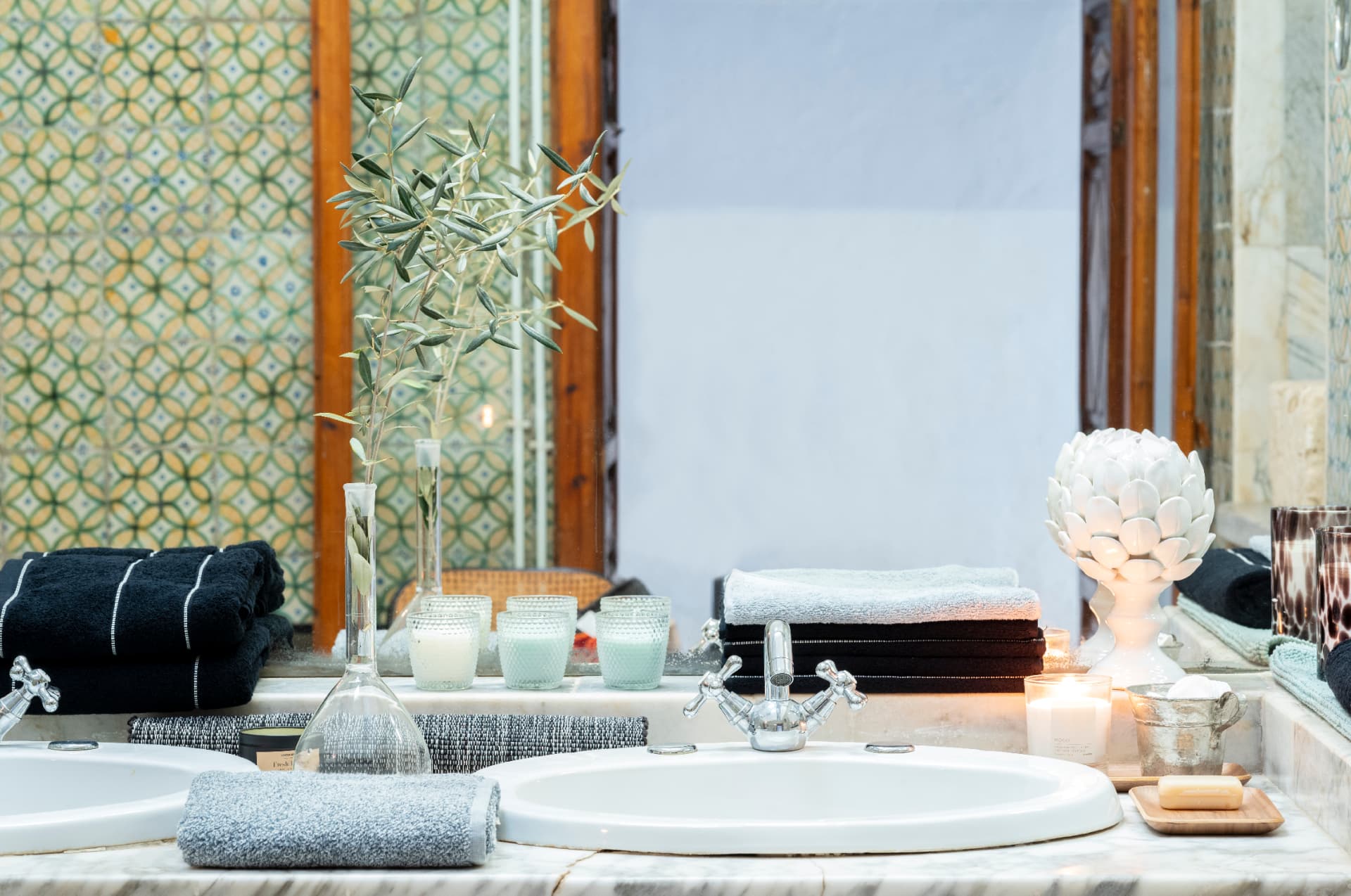 Bathroom sinks with stacked towels, an olive branch in a decanter and a mirror