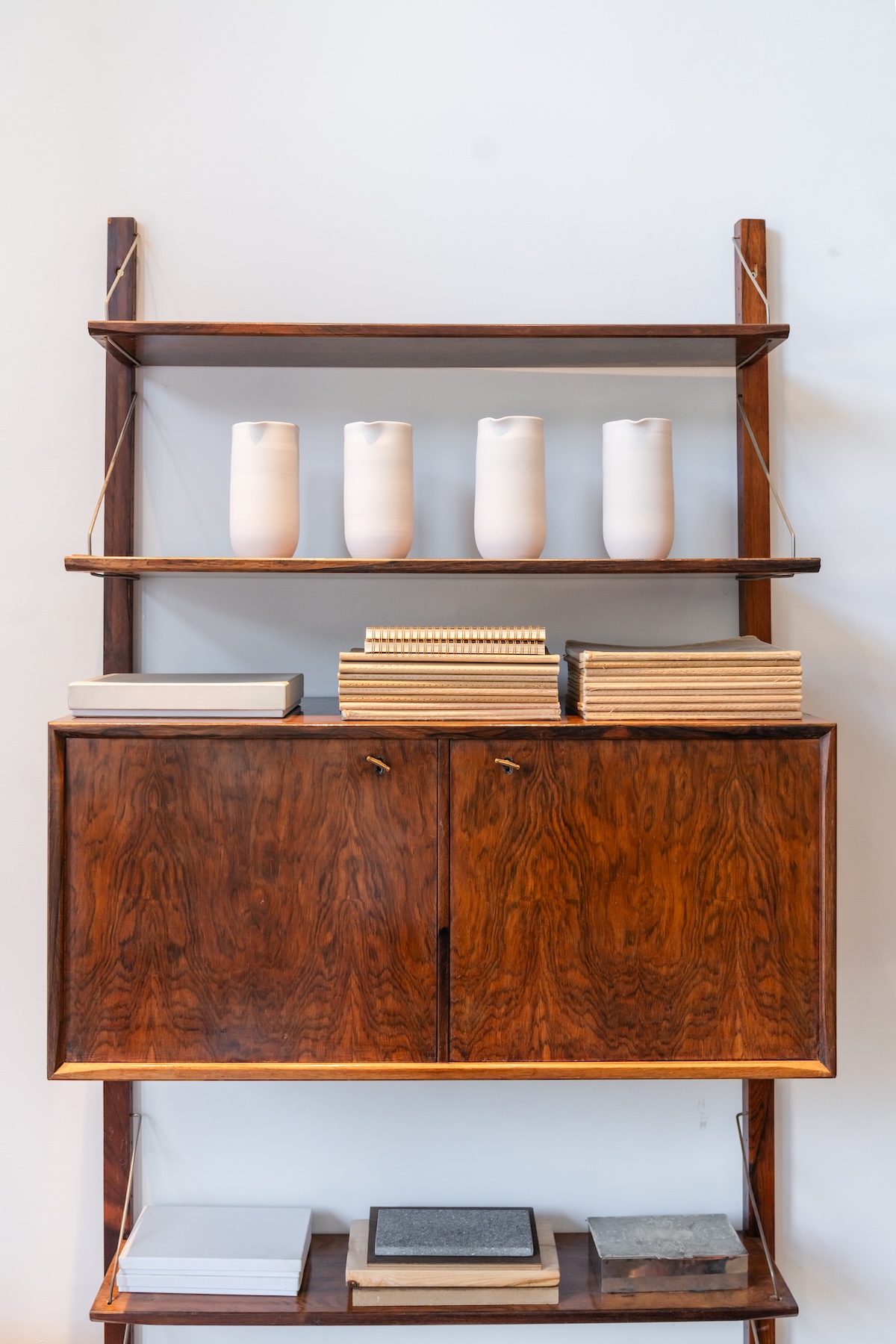 Rosewood wall shelving with white ceramic pitchers and stacked books