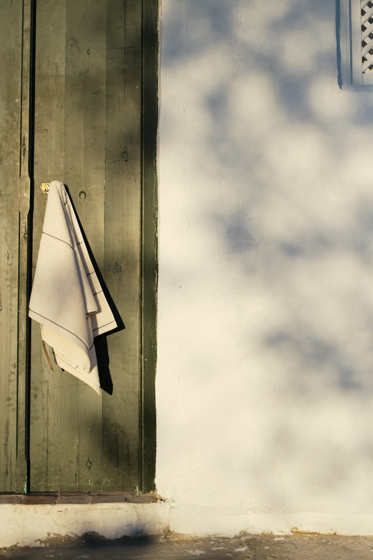 Cream towel hanging on a green wooden door against a sunlit white wall