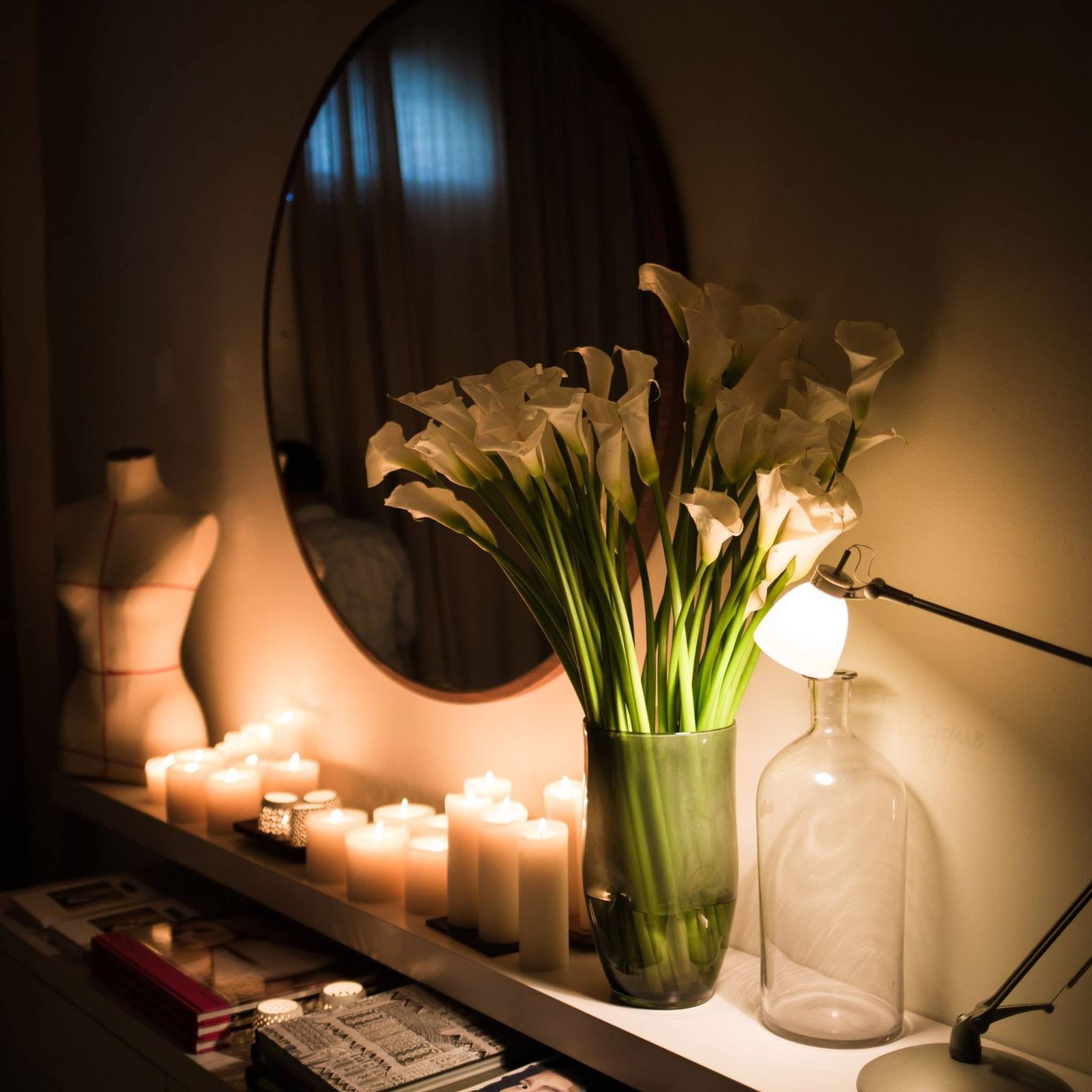 White calla lilies and candles arranged beneath a round mirror