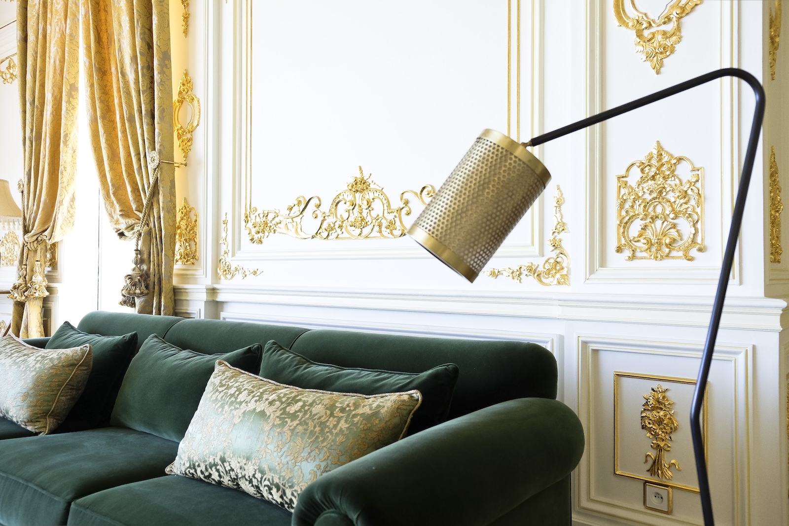 Green velvet sofa beneath a sculptural brass floor lamp
