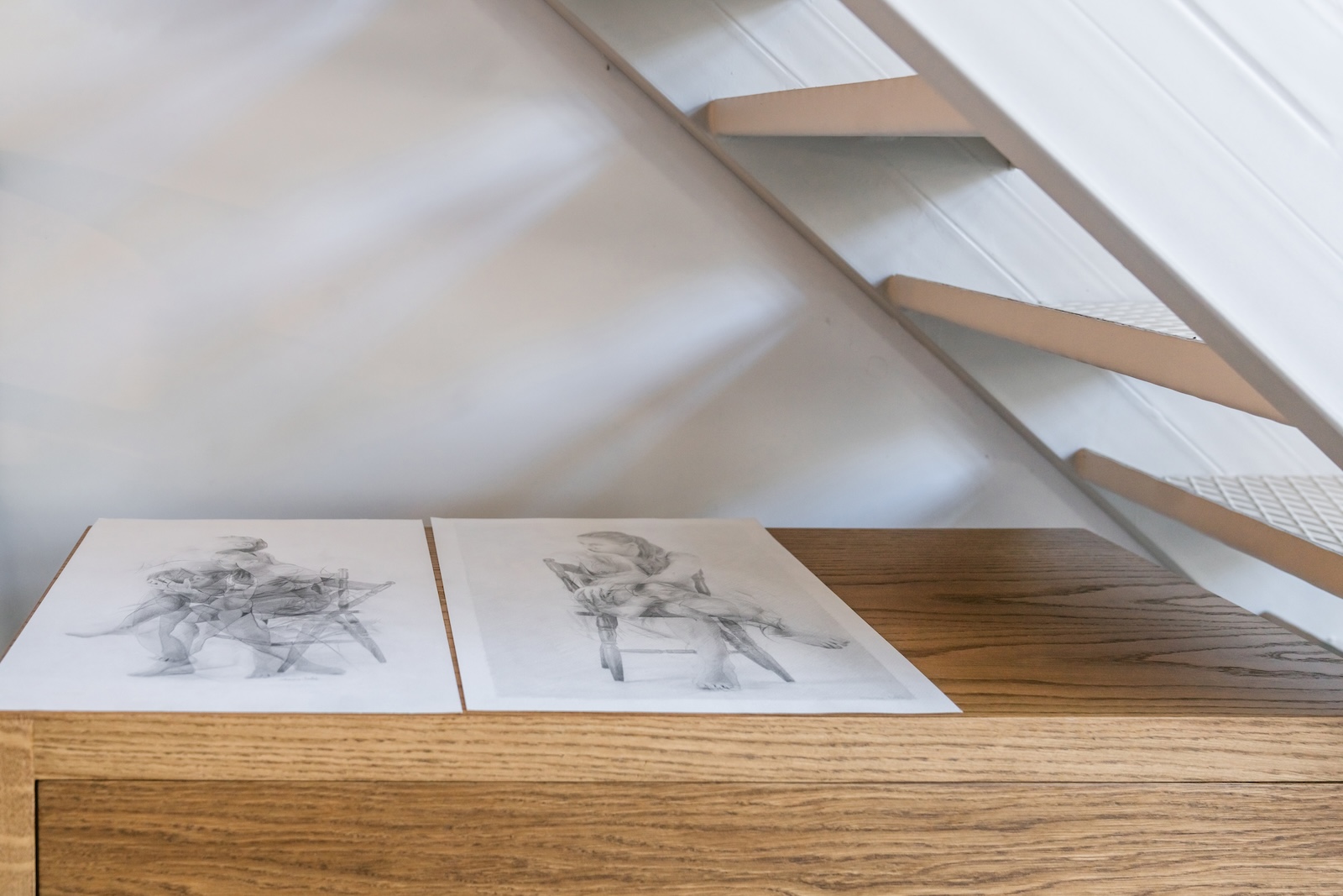 Sketches laid on an oak bench beneath a white staircase