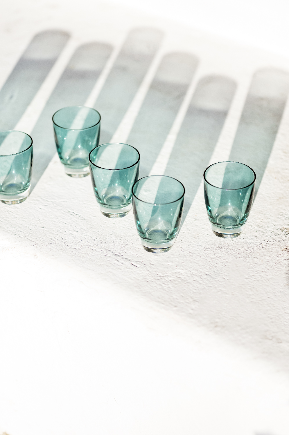 Blue drinking glasses on a white surface with striped shadows