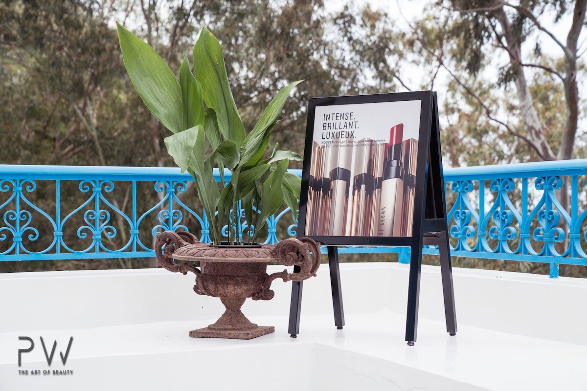 Bobbi Brown campaign easel beside a planted urn on a terrace with blue railing