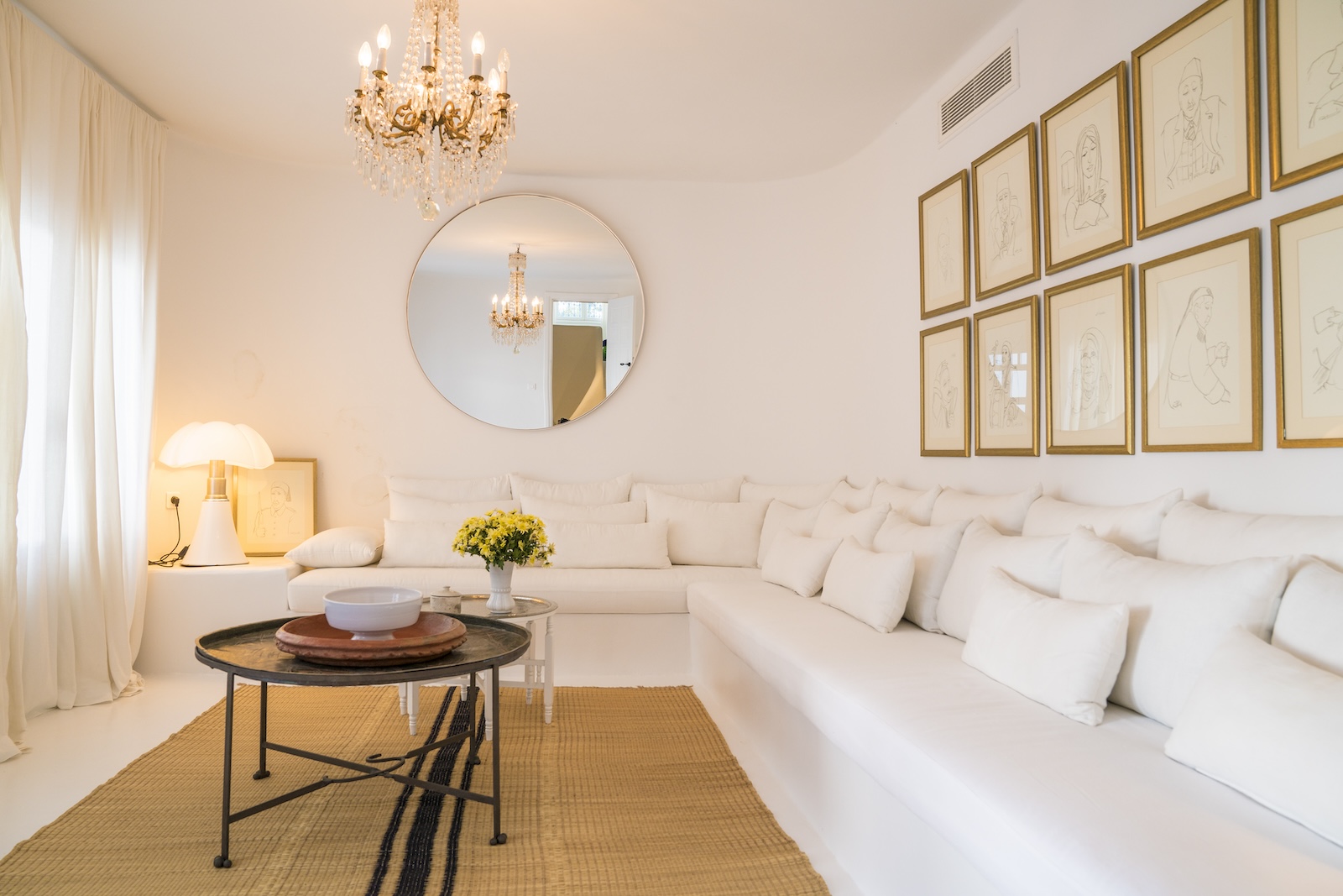 White lounge with a built-in corner sofa, framed line drawings and a crystal chandelier